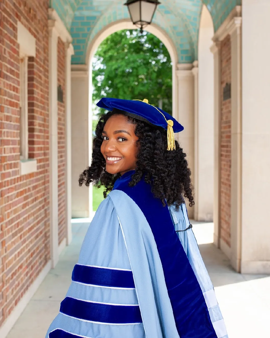 Aliyah Griffith in her doctoral cap and gown beneath a brick archway
