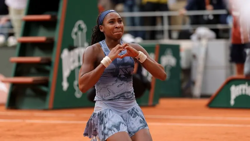Coco Gauff makes a heart shape with her hands on the clay court at Roland-Garros